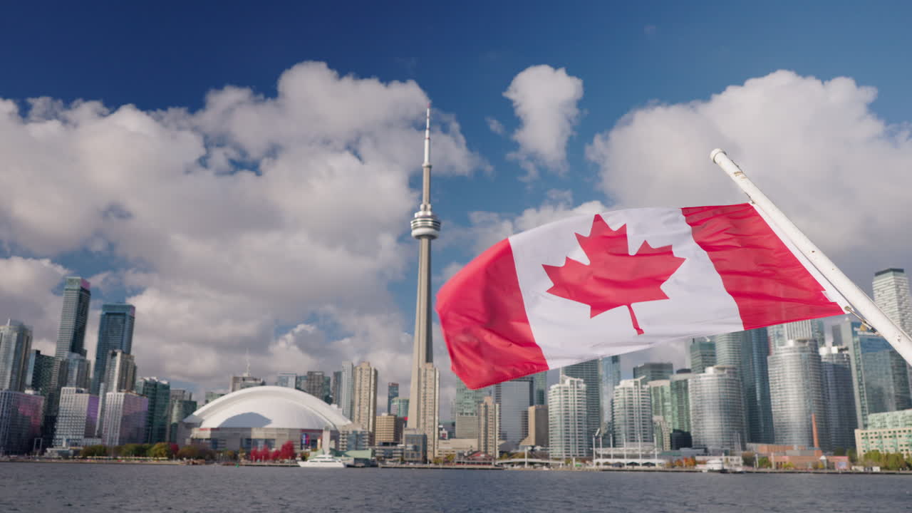 Bandiera canadese che sventola su una barca con lo skyline e il lungomare di Toronto, moderni edifici cittadini sul Lago Ontario sotto un cielo luminoso con nuvole
