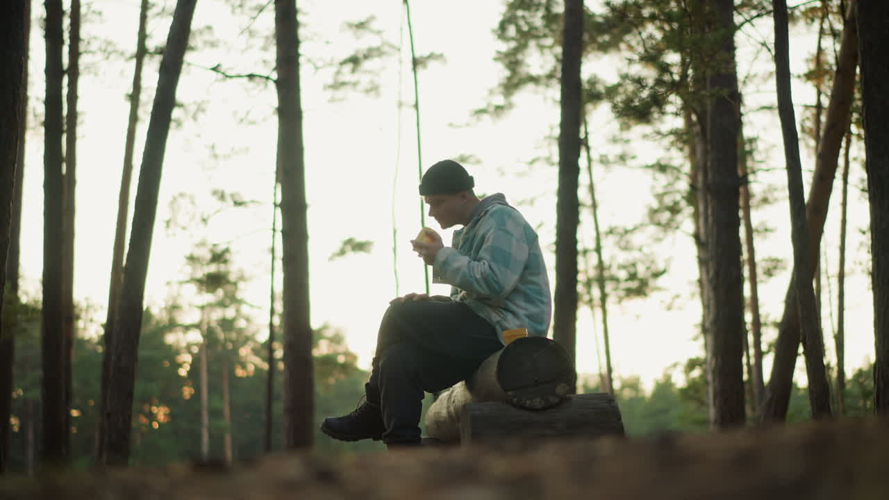 sunlit hiker sipping coffee on log, backlit pine silhouettes at sunrise, warm rim light, thermos in hands, backpack leaning on log, contemplative gaze toward horizon, travel momentum, fresh air