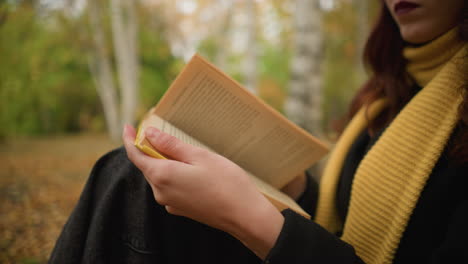 close-up of woman with yellow scarf flipping through book pages thoughtfully, autumn leaves cover the ground as she reads in a tranquil outdoor setting, immersed in the moment with focus