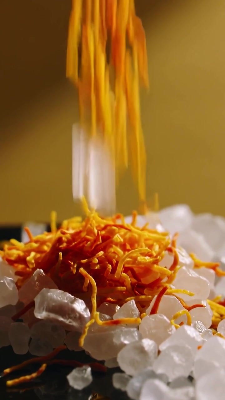 Vertical video: Falling saffron threads forming nest on white crystal pile on studio plate