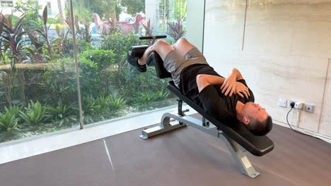 Joven-Asiático-Haciendo-Abdominales-En-Un-Lujoso-Gimnasio-De-Alta-Gama-Con-Una-Vista-Panorámica-De-La-Ventana