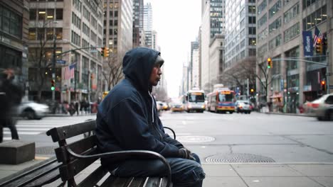 a solitary individual sits quietly on a bench in a busy city, observing the fast-moving buses and pedestrians around them. the scene captures urban life and loneliness.