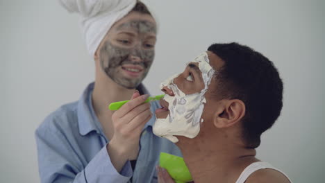 Mujer-Con-Máscara-Facial-Aplicando-Exfoliante-A-Un-Apuesto-Hombre-Negro-1