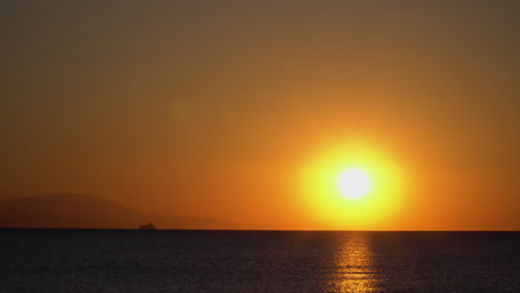 Beautiful-and-calm-static-shot-of-a-sunrise-with-boat-and-mountains-on-horizon