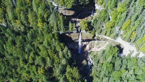 Birds-eye-view-of-an-isolated-waterfall-flowing-vertically-from-steep-rocky-walls-amidst-thick-dense-forest