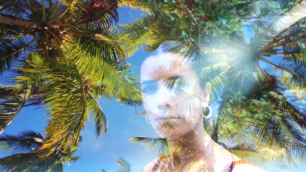 Ritratto artistico a doppia esposizione di una donna fuso con palme tropicali e acqua blu cristallina.