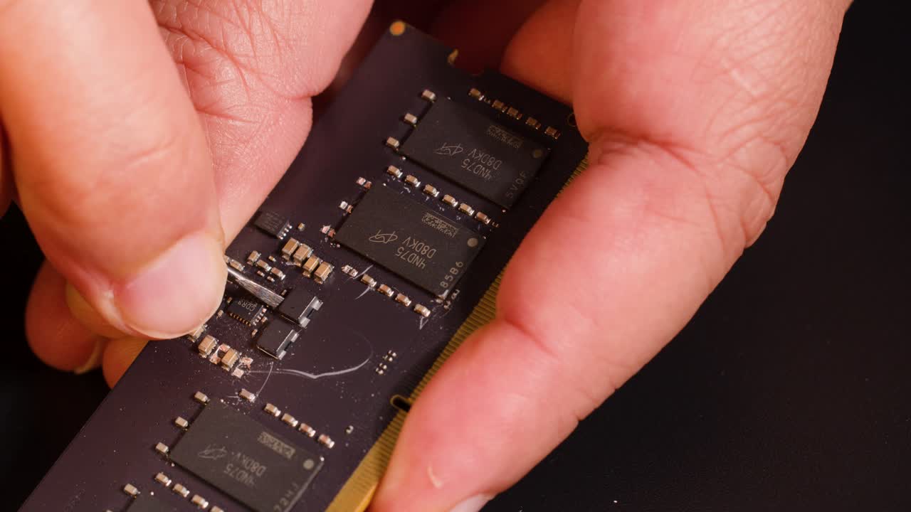 Close-up shot of hands using a metal tool to inspect a computer memory circuit board