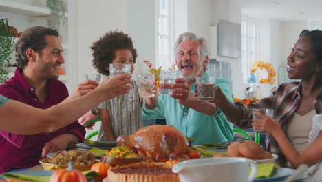 Familia-Multigeneracional-Celebrando-El-Día-De-Acción-De-Gracias-En-Casa-Comiendo-Y-Animando-Con-Agua