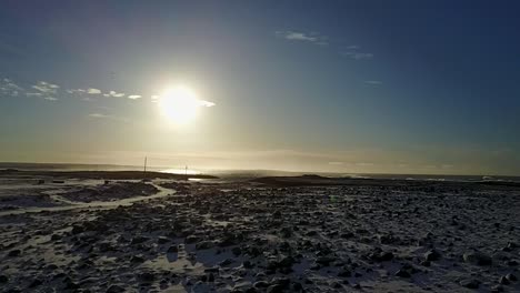 Aerial-flight-moving-rapidly-to-shore-over-snowy-rock-terrain-in-Keflavik,-Iceland