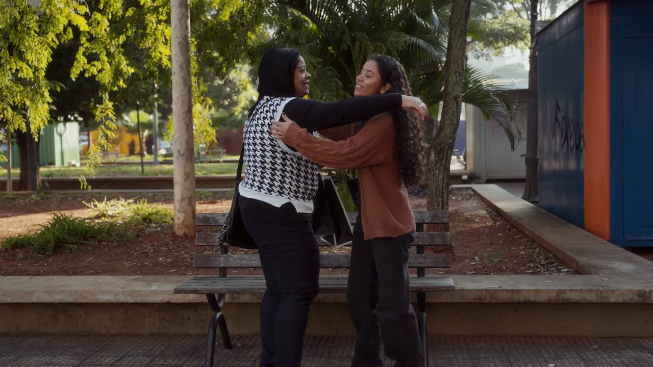 Two women having a friendly conversation and sharing shopping bags and coffee in a park