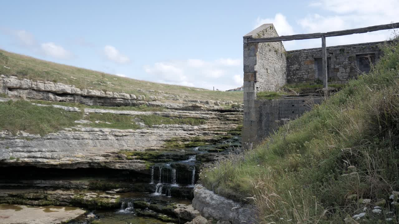 Ruins of Bolao Windmill in Cantabria, Spain, with a flowing stream beside it