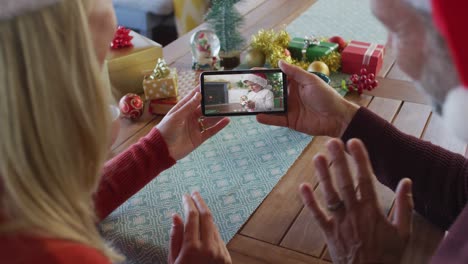 pareja caucásica con sombreros de santa usando un teléfono inteligente para una videollamada de navidad con un niño en la pantalla