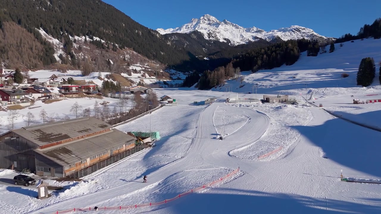 Luftfoto af Savognin skiområde i de schweiziske alper med skiløbere på sneklædte pister og alpelandsby omgivet af bjerge under klar vintersol i Graubünden, Schweiz. Vidvinkelbillede.