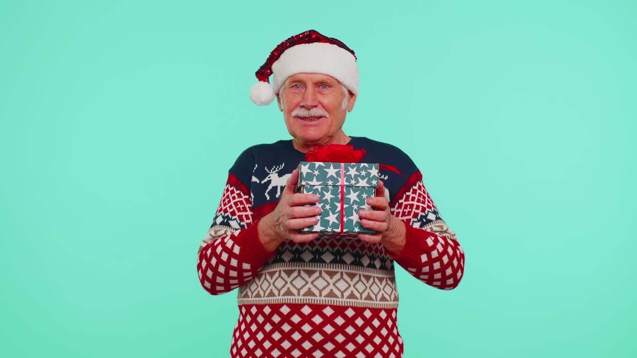 Grandfather in santa sweater presenting one christmas gift box stretches out his hands to camera