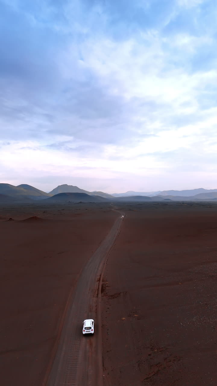 Approaching a white car riding by the ground road in the deserted mountainous landscape. Scenery of a rocky area in Iceland. Vertical video.
