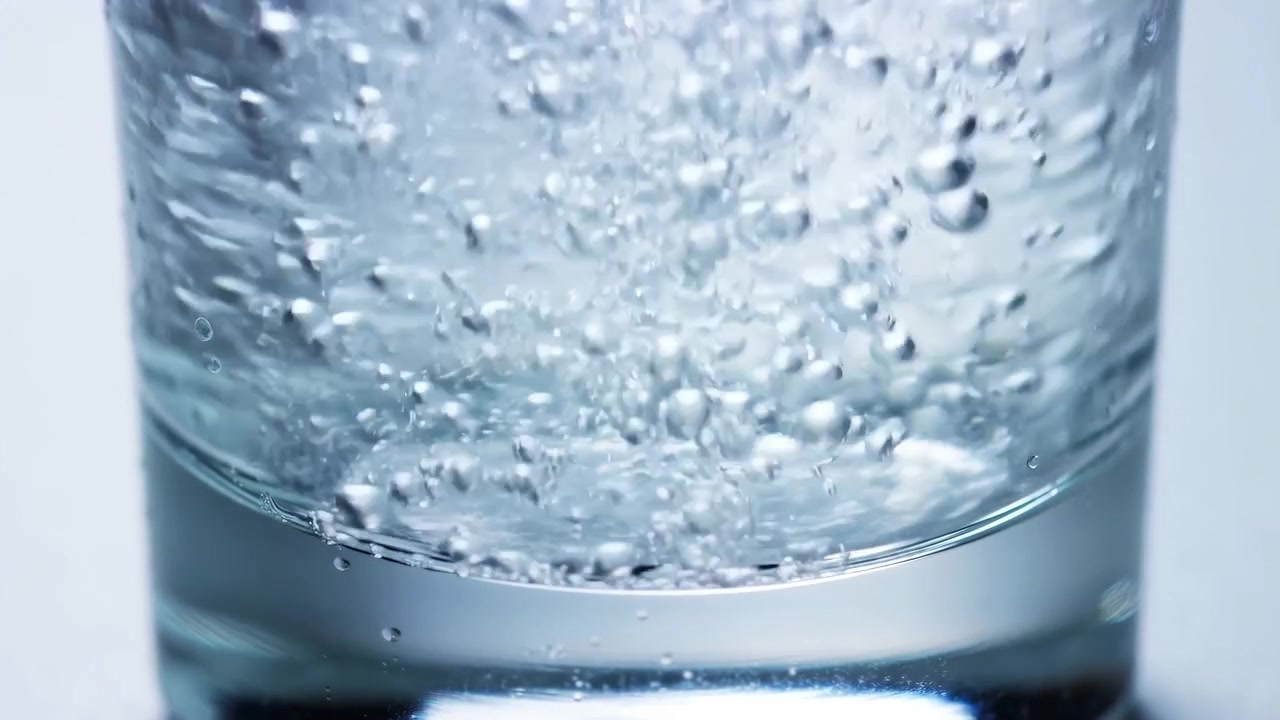 Bicchiere con bollicine di acqua frizzante in ascesa, macro ravvicinata di liquido effervescente, condensa sulla superficie interna.