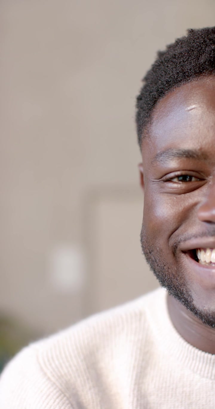 Vidéo verticale : Homme afro-américain ouvrant les yeux, souriant à la caméra, en pull dans une pièce, avec espace pour texte