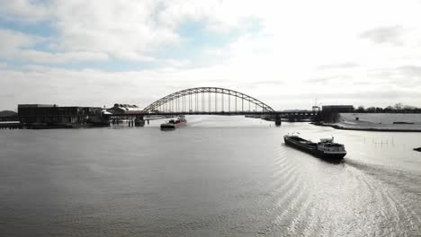 freight vessels crossing under the bridge of river noord in netherland against bright cloudy sky. - aerial wide shot