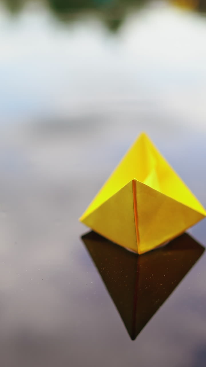 Woman's hand launches paper boat on the water. Paper boat sails along the river. Vertical video