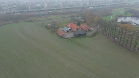 High-aerial-of-small-farm-with-a-city-covered-in-mist-in-the-background