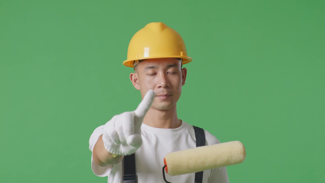 Close Up Of Asian Man Painter Wearing Safety Helmet Pointing At You And Disapproving With No Index Finger Sign While Standing In The Green Screen Background Studio