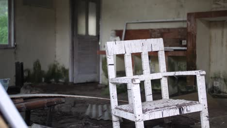 A-single-white-chair-is-standing-by-itself-in-a-creepy,-dirty,-dusty-and-abandoned-room-full-of-dirt,-junk-and-trash