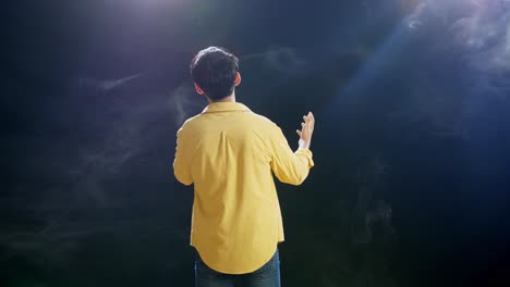 vista trasera de un niño con un micrófono en la mano y cantando sobre el fondo blanco de humo negro