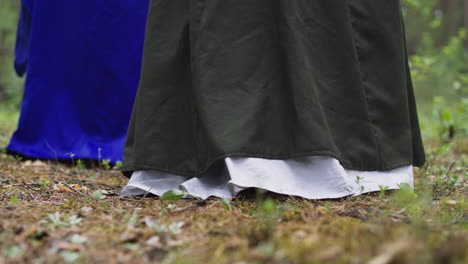 women in long vintage dresses walk through forest in spring