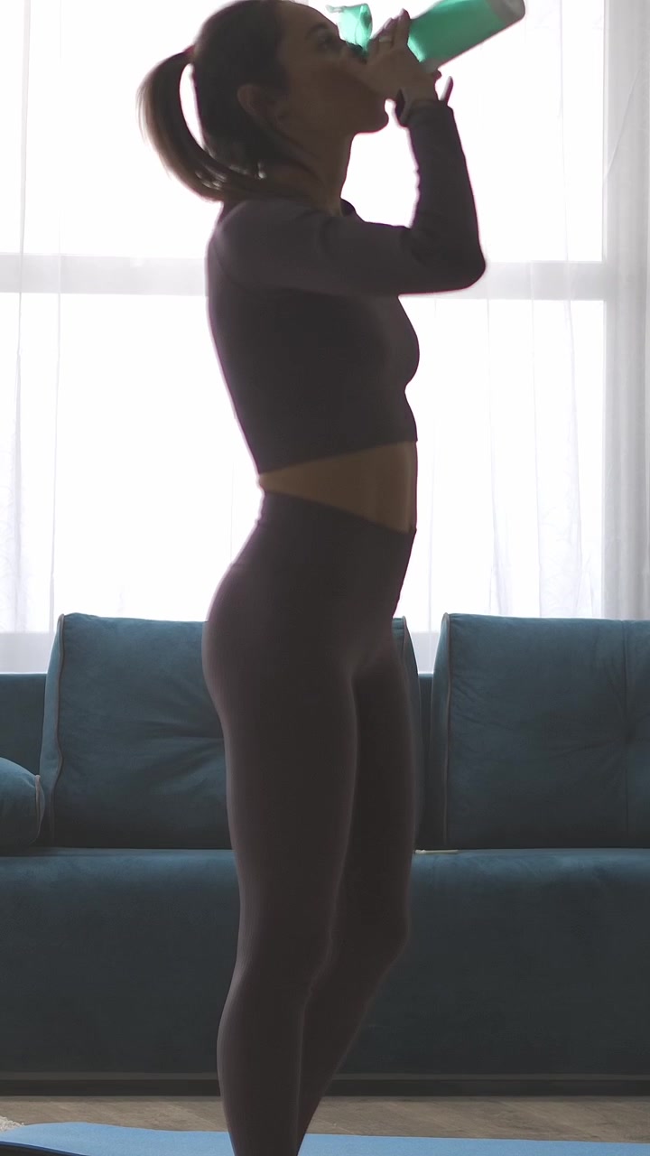 Donna in forma che fa stretching e beve acqua dopo un allenamento a casa.