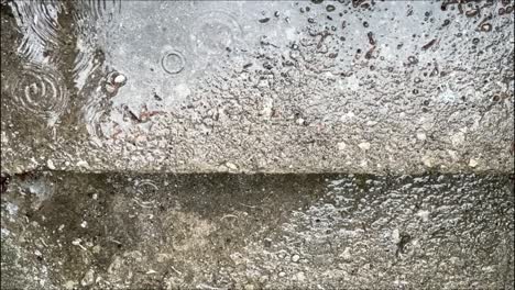 Gotas-De-Lluvia-Sobre-Suelo-De-Hormigón-Con-Reflejos-En-Charcos