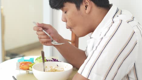 side view of young asian man blowing on hot instant noodles while eating with fork