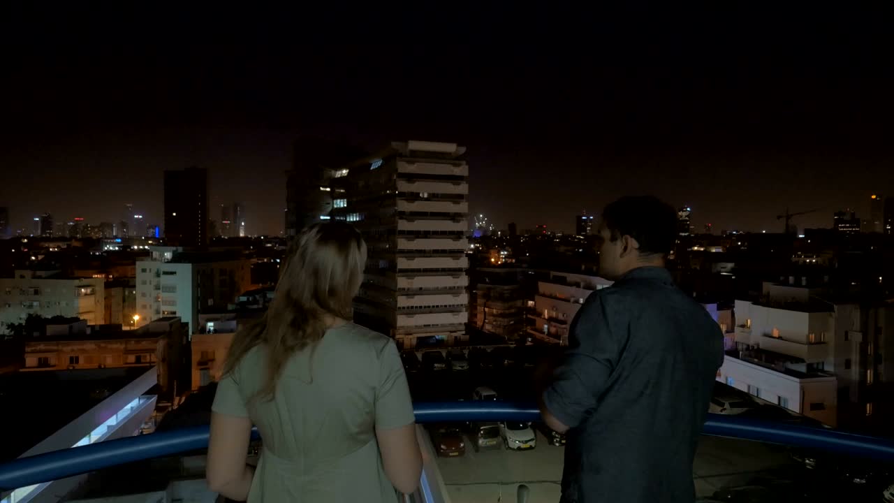 남자 와 여자 가 호텔 지붕 에서 밤 에 텔아비브 를 바라보고 있다