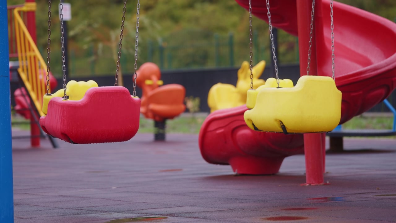 Altalena rossa bagnata che dondola nel parco giochi