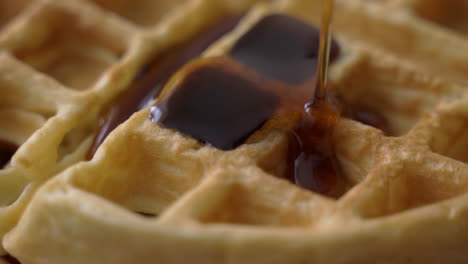 Drehende-Makroansicht-Aus-Nächster-Nähe-Von-Knusprigen,-Goldenen-Waffeln,-Die-Zum-Morgendlichen-Frühstück-Mit-Süßem-Ahornsirup-Beträufelt-Werden