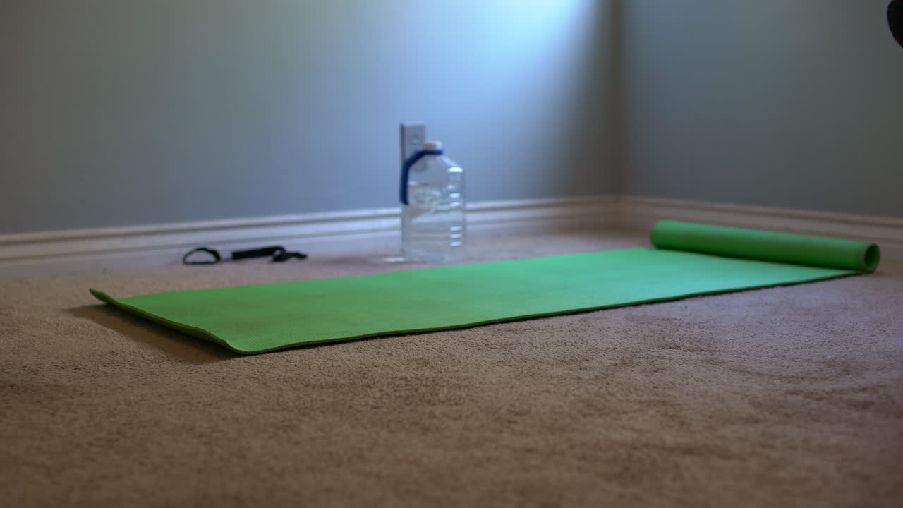 zoom en una toma media de una alfombra de yoga verde, correa de alfombra de yoga y botella de agua para representar un entrenamiento en casa