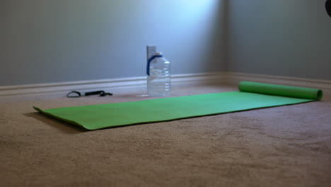 Zoom-in-medium-shot-of-of-a-green-yoga-mat,-yoga-mat-strap,-and-water-bottle-to-represent-a-home-workout