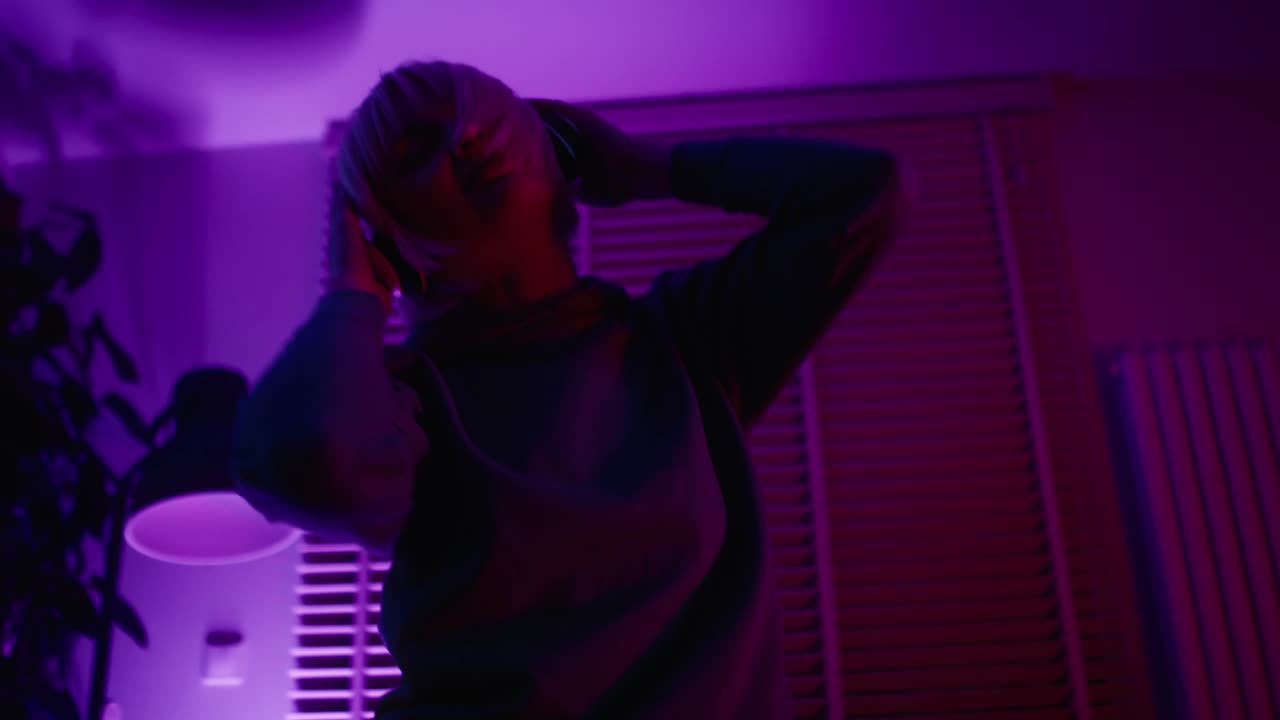 Giovane donna caucasica che balla in casa tra luci al neon