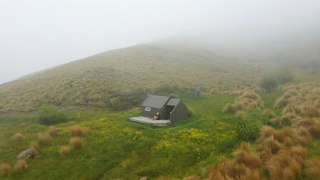 hiker relaxing on deck of a hut within tussock grass covered hills in new zealand