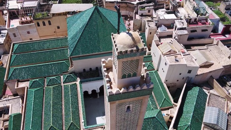 Prospettiva ravvicinata e sopraelevata da drone che cattura l'intricato minareto intagliato e i vivaci tetti a piramide con tegole verdi di una moschea storica a Fez, Marocco