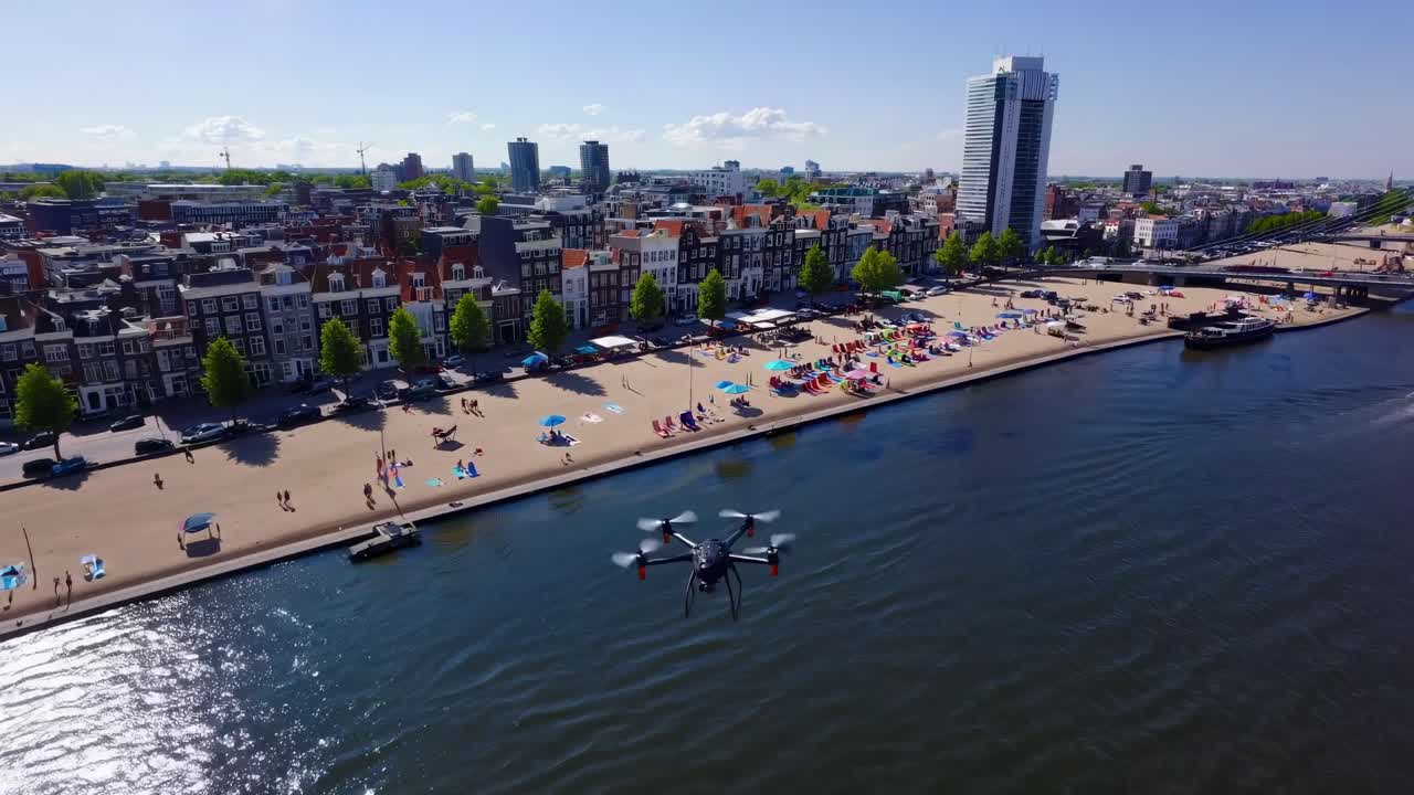 Drone capturing vibrant Amsterdam beach and Amstel river on a sunny summer day, featuring colorful beach chairs, umbrellas, and a backdrop of traditional and modern architecture