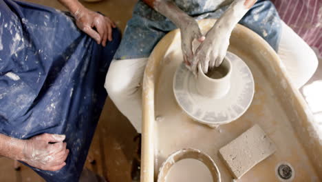 hands of diverse male potters using potter's wheel in pottery studio, slow motion