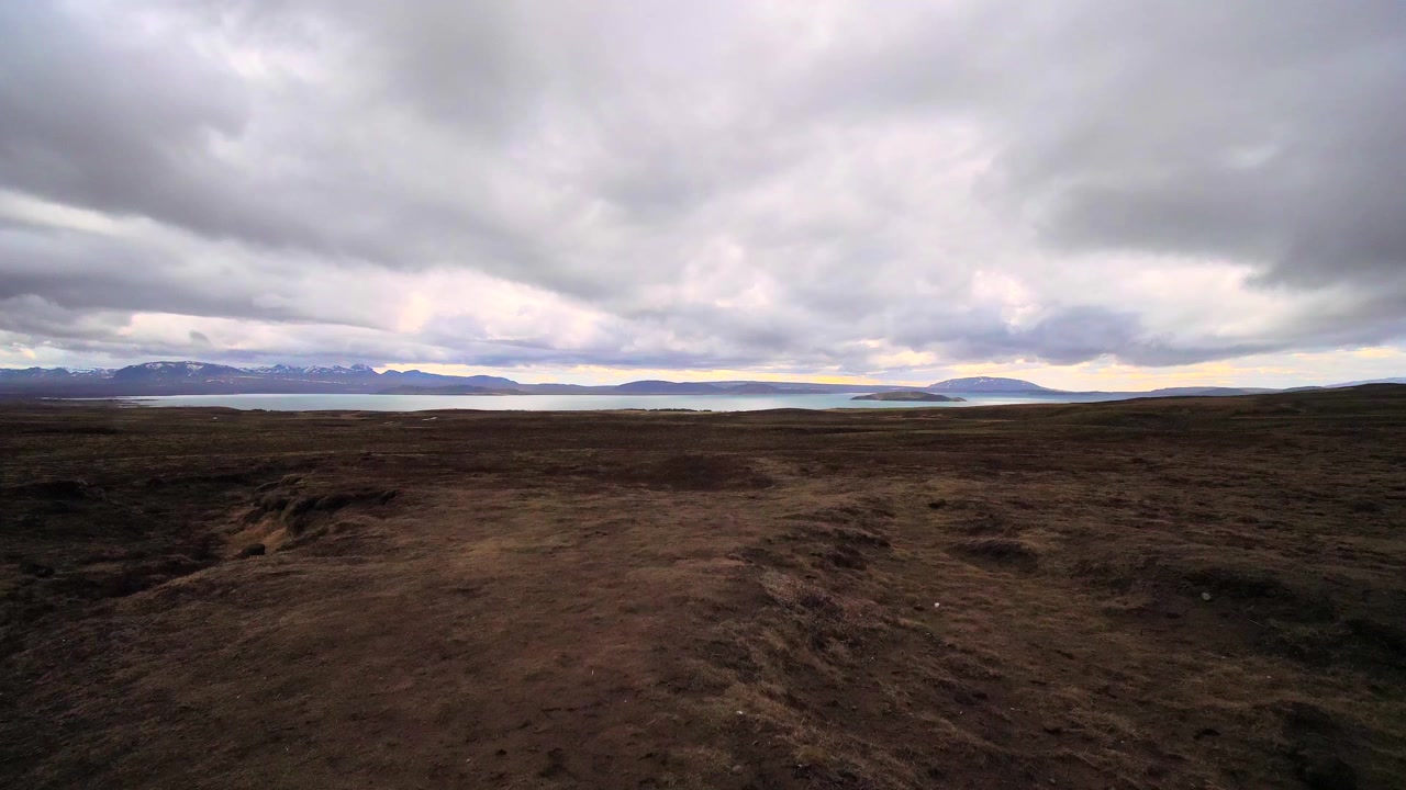 Dark highland landscape stretching toward distant mountains beneath heavy clouds with soft sunset light along the horizon in Iceland