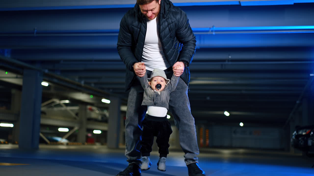 Father rises his cute little baby boy in hands. Dad plays with his infant son with pacifier in mouth. Low angle view.