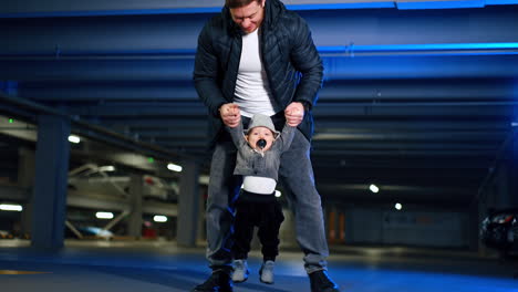 father rises his cute little baby boy in hands. dad plays with his infant son with pacifier in mouth. low angle view.
