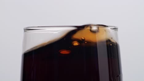 close up of ice cubes falling in a glass of fresh cola on white background