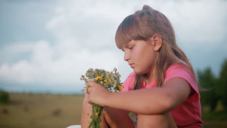 la niña mira pensativa a las flores en su mano mientras está sentada en el campo rural, la suave luz del sol destaca su expresión mientras admira los delicados pétalos con vastas tierras de cultivo