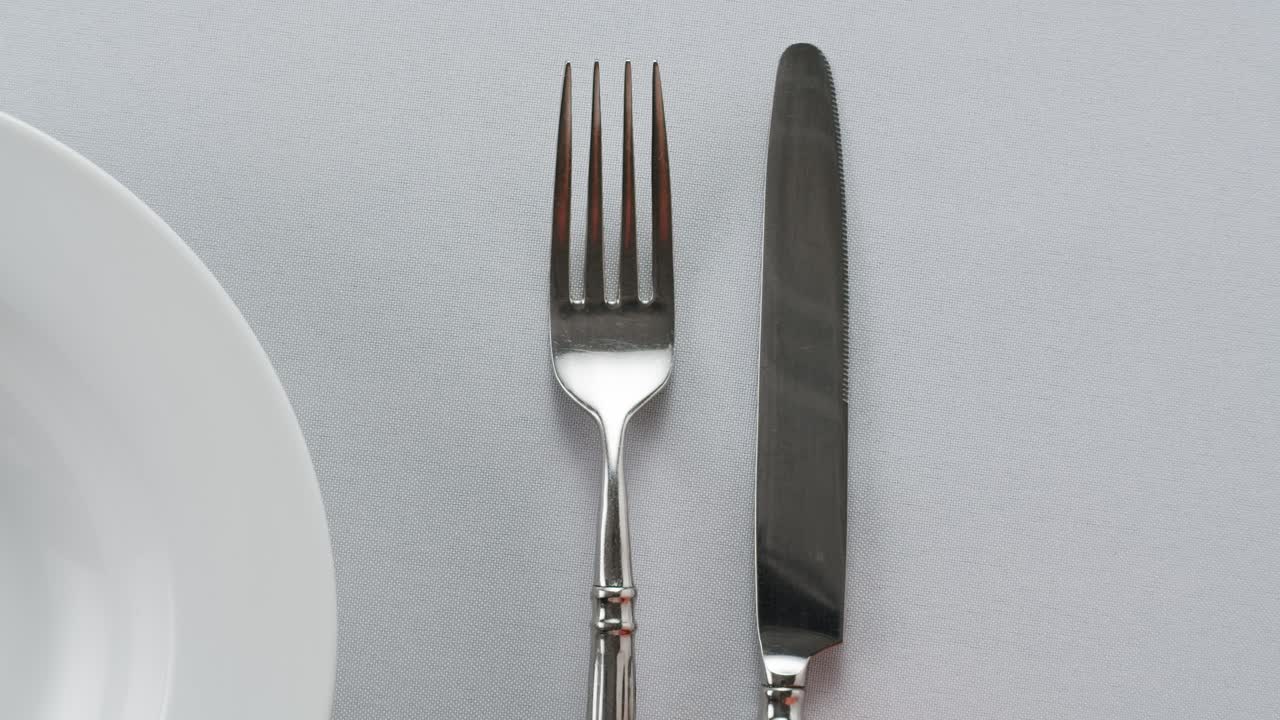 Professional table setting with white gloves. Plates, fork, knife, and glass arranged on a white table.