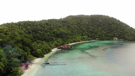 An-aerial-view-of-the-serene-beauty-of-a-tropical-coastline-of-Kri-Island-in-Raja-Ampat-archipelago,-Indonesia,-with-lush-green-forest-meeting-crystal-clear-turquoise-waters