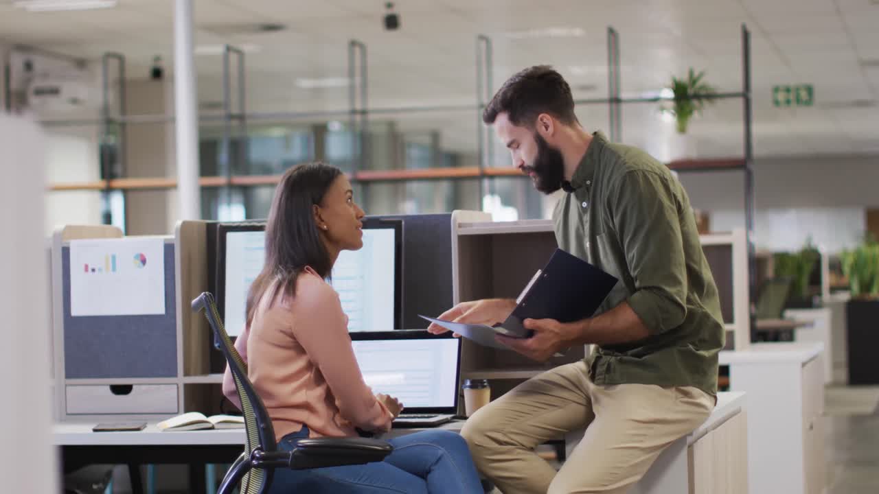 video de una mujer de negocios diversa y un hombre de negocios usando una computadora portátil y hablando en la oficina