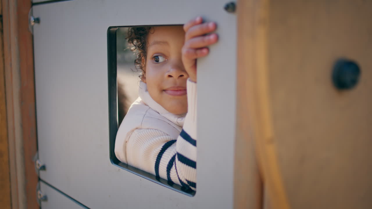 Curly kid playing in toy house closeup. Cute girl looking from window